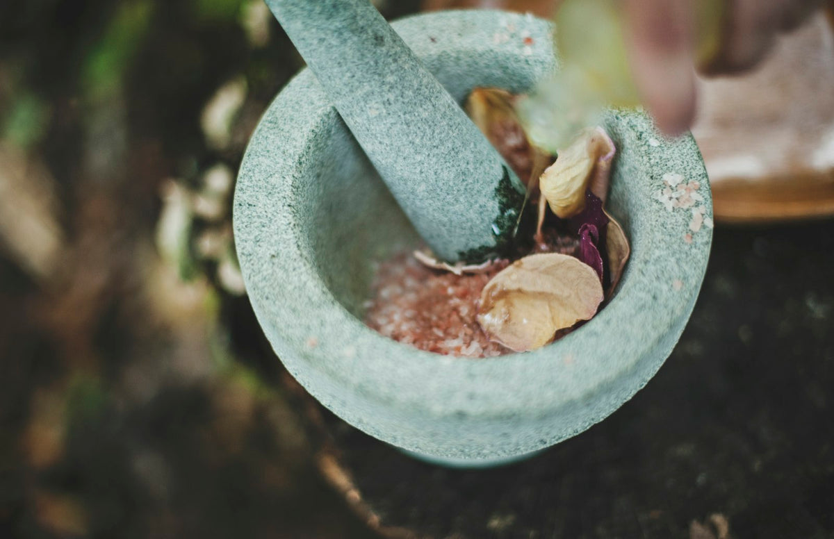 A grey stone mortar and pestle holding coarse pink salt and dried flower petals, seen from above