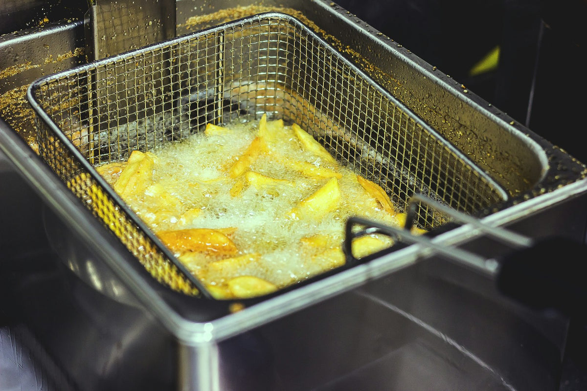 Chips frying in a wire basket of hot oil