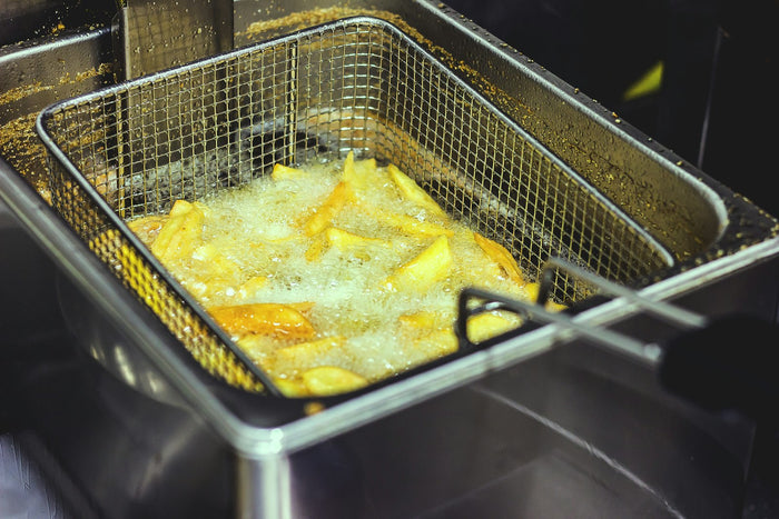 Chips frying in a wire basket of hot oil