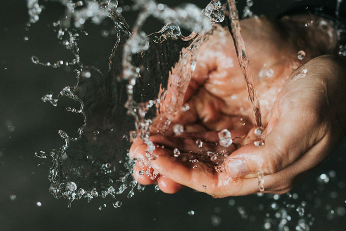 A stream of water splashing into a pair of cupped hands against a dark background
