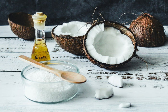 Halved coconuts beside a jar of coconut oil and flakes