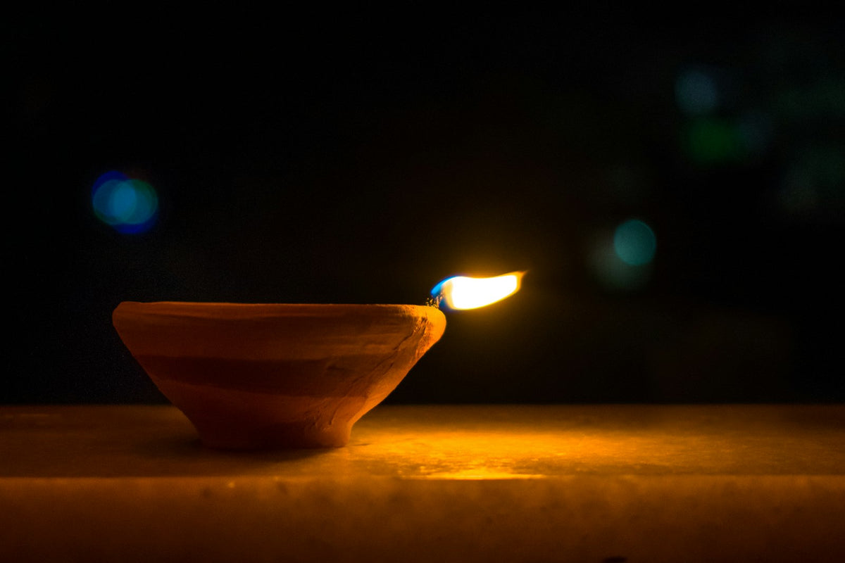 A lit clay diya on a wooden surface