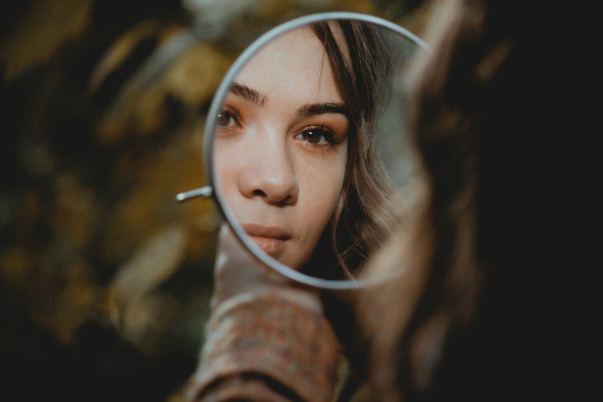 A young woman's eyes, nose and the skin beneath her eyes reflected in a small round hand mirror