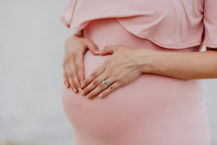 A pregnant woman in a pink dress with her hands on her belly