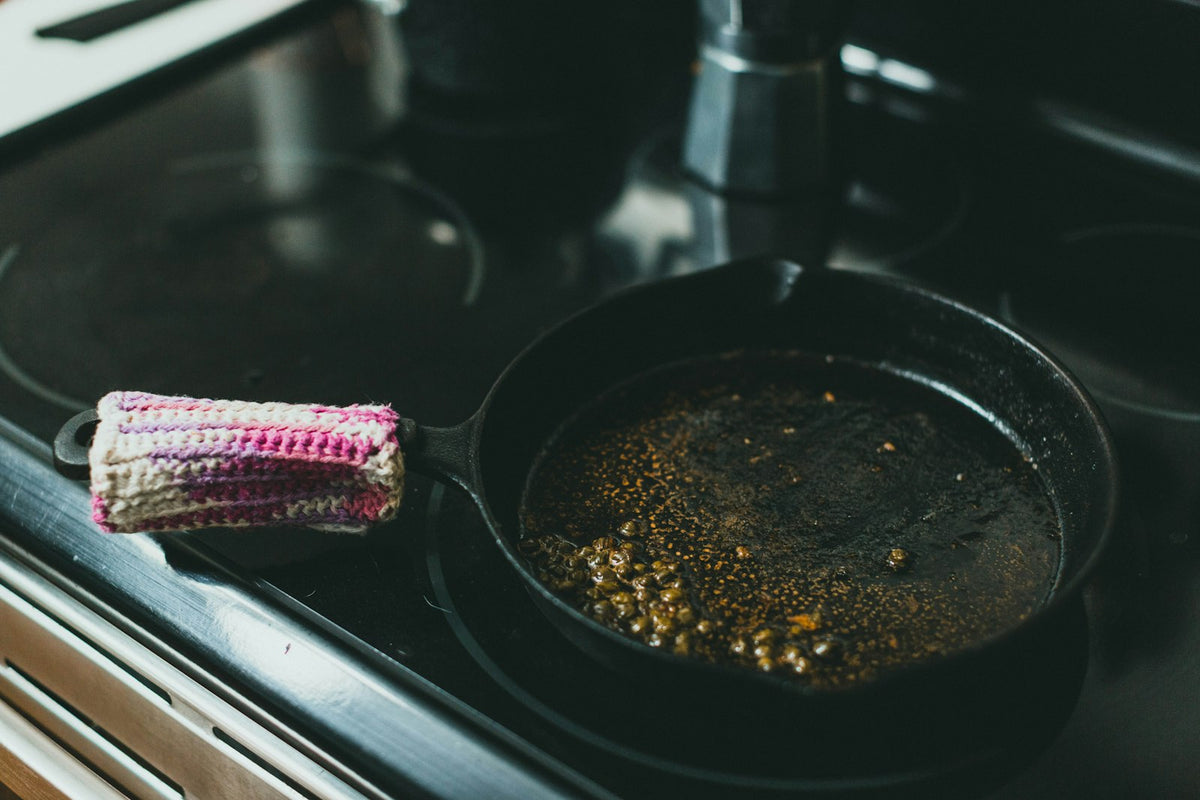 A black frying pan with browned crumbs on a hob