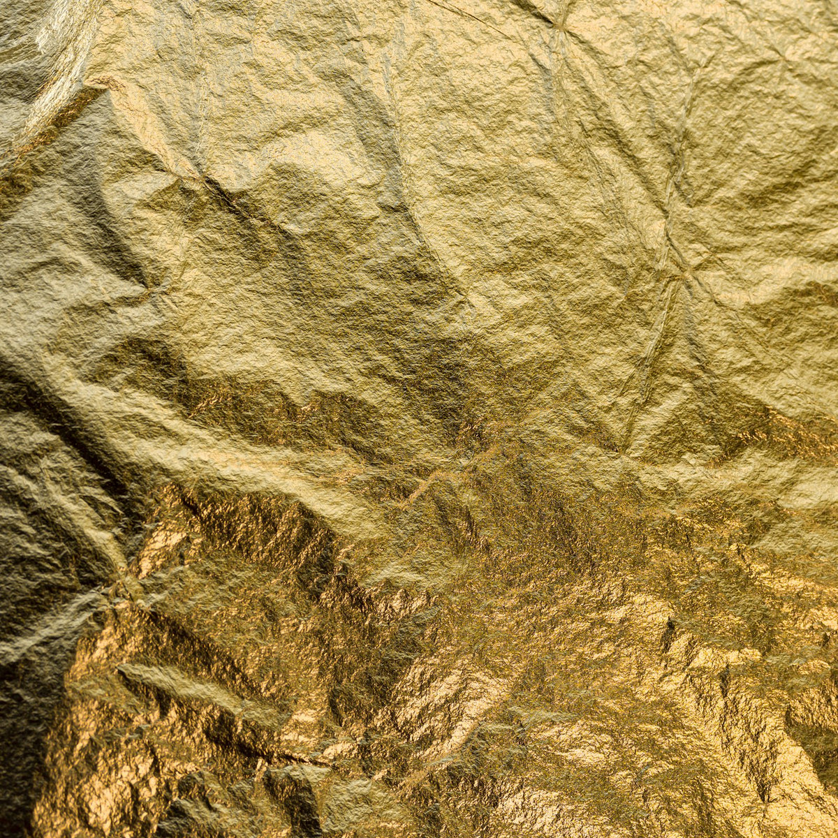 A sheet of crumpled gold leaf filling the frame, creased and glinting under soft light