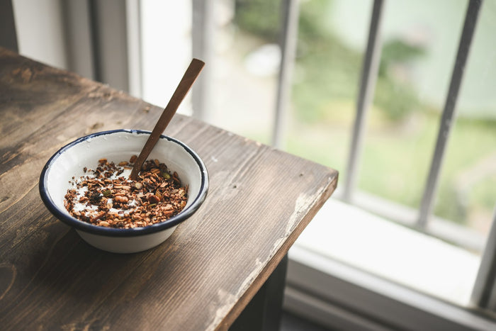 A bowl of yogurt and granola on a table by a window