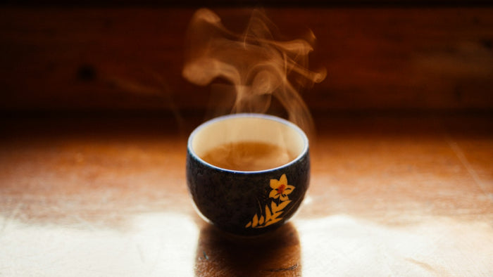 Steam rising from a dark blue ceramic cup of tea with a yellow flower motif on a warm wooden table