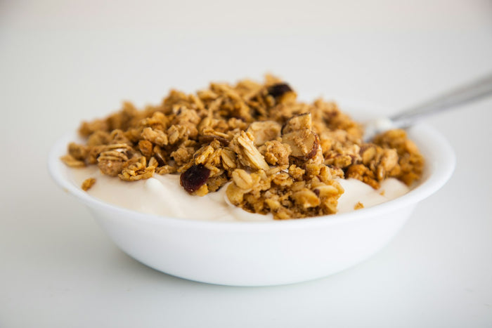 A white bowl of plain yoghurt topped with oat and nut granola, a spoon resting in it