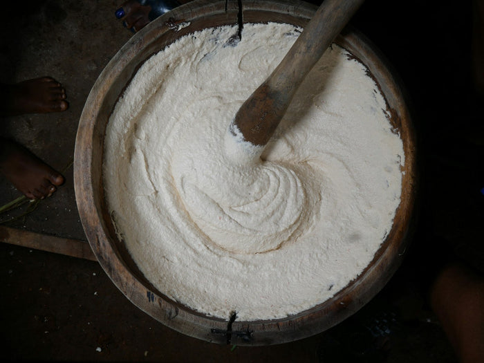 A wooden churn paddle resting in a pot of curd