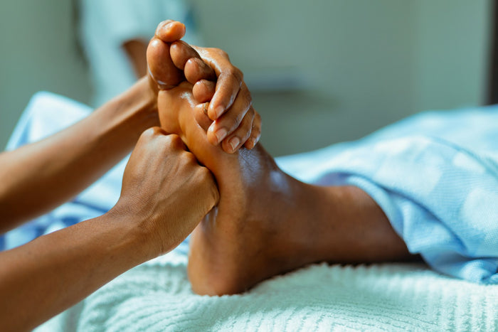 Two hands massaging the sole of a bare foot resting on a white towel