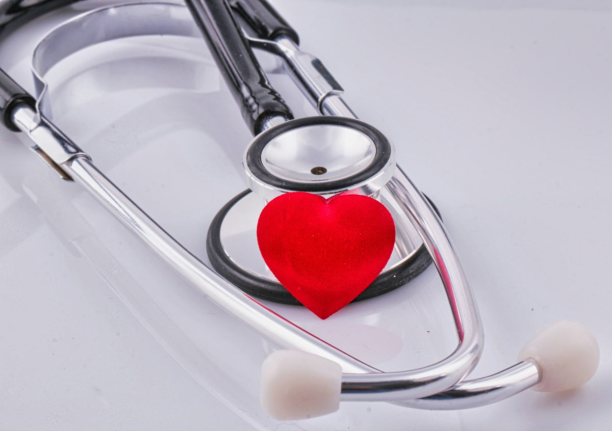 A small red fabric heart resting against the chest piece of a silver and black stethoscope on a white surface