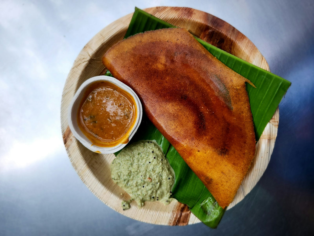 A folded golden-brown dosa on a banana leaf in a leaf plate, with a cup of sambar and a spoonful of coconut chutney