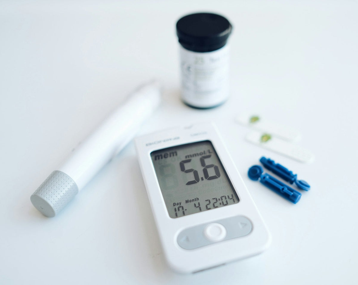 A blood glucose meter beside test strips and a lancet