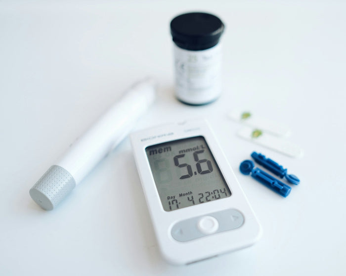 A blood glucose meter beside test strips and a lancet