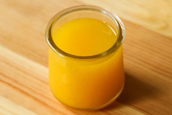 A small glass jar of golden ghee on a wooden table