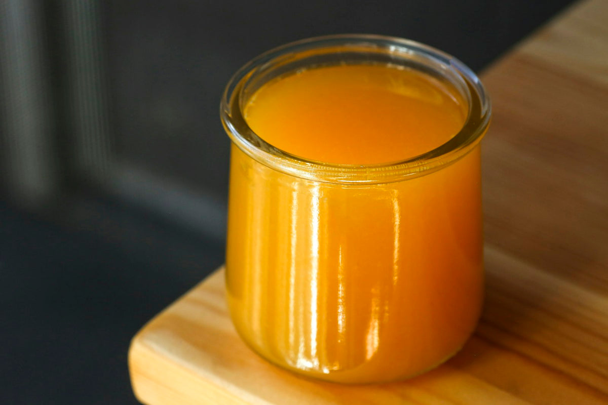 A glass jar of golden liquid ghee on a wooden board
