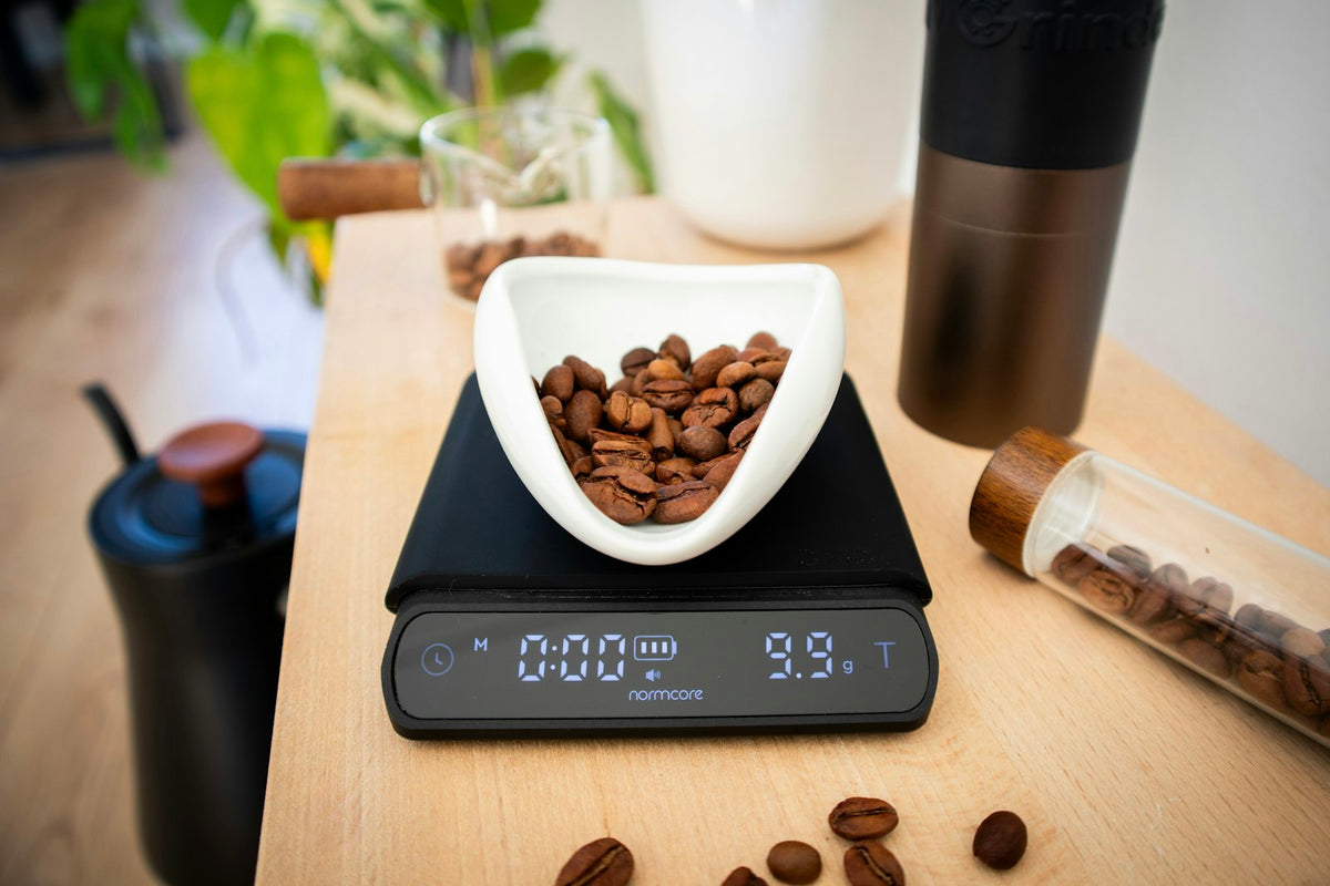 A digital kitchen scale weighing coffee beans in a dish