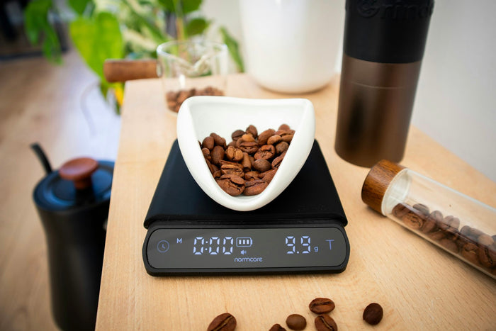 A digital kitchen scale weighing coffee beans in a dish
