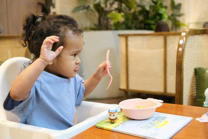 A toddler eating from a bowl in a high chair