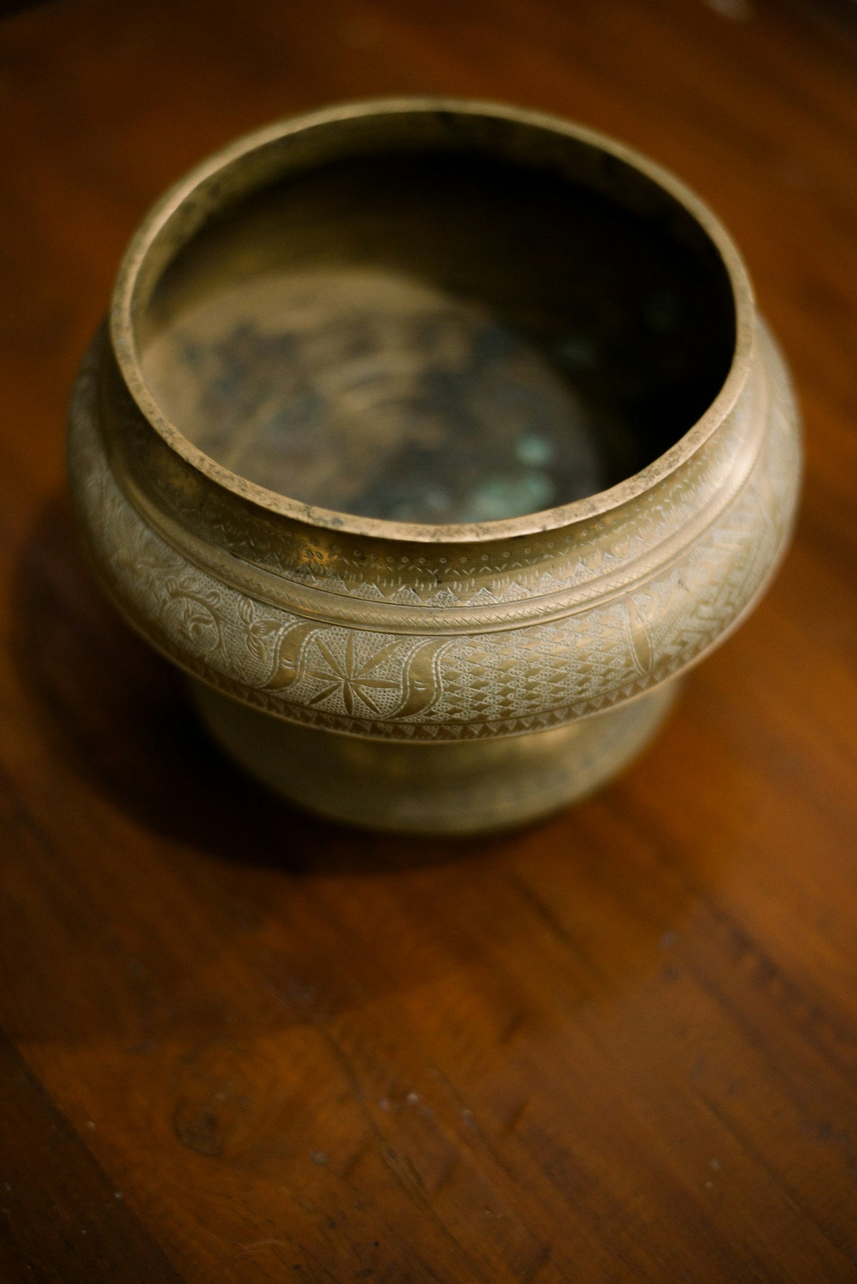 An empty engraved brass pot on a wooden table