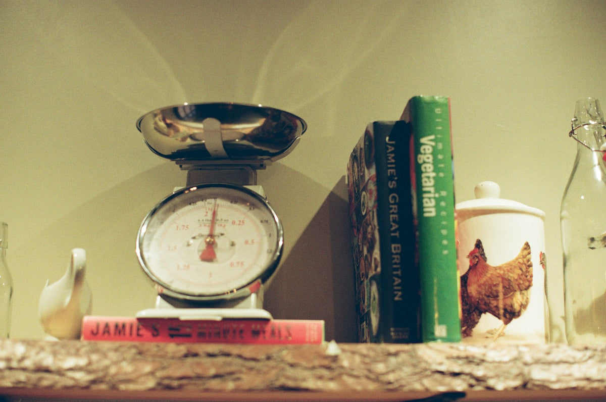 An old dial kitchen scale on a shelf with cookbooks