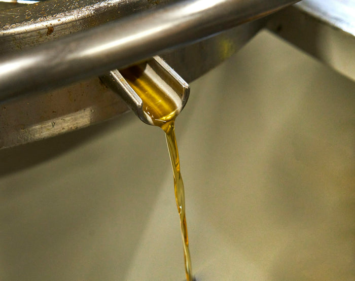 A thin stream of golden oil pouring from a metal spout on stainless steel equipment