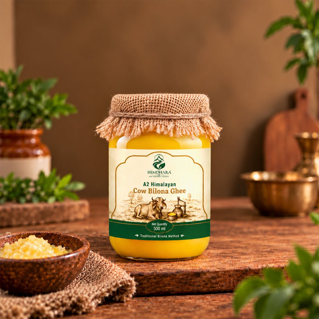 Himdhara A2 Cow Bilona Ghee 500 ml jar with a jute cloth lid, among fresh herbs and brass bowls